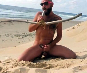 fellow plows himself on the beach with a wooden faux-cock